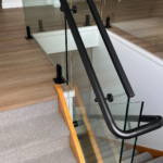 Modern staircase glass panels with black handrail installed by Shine Glass Australia.